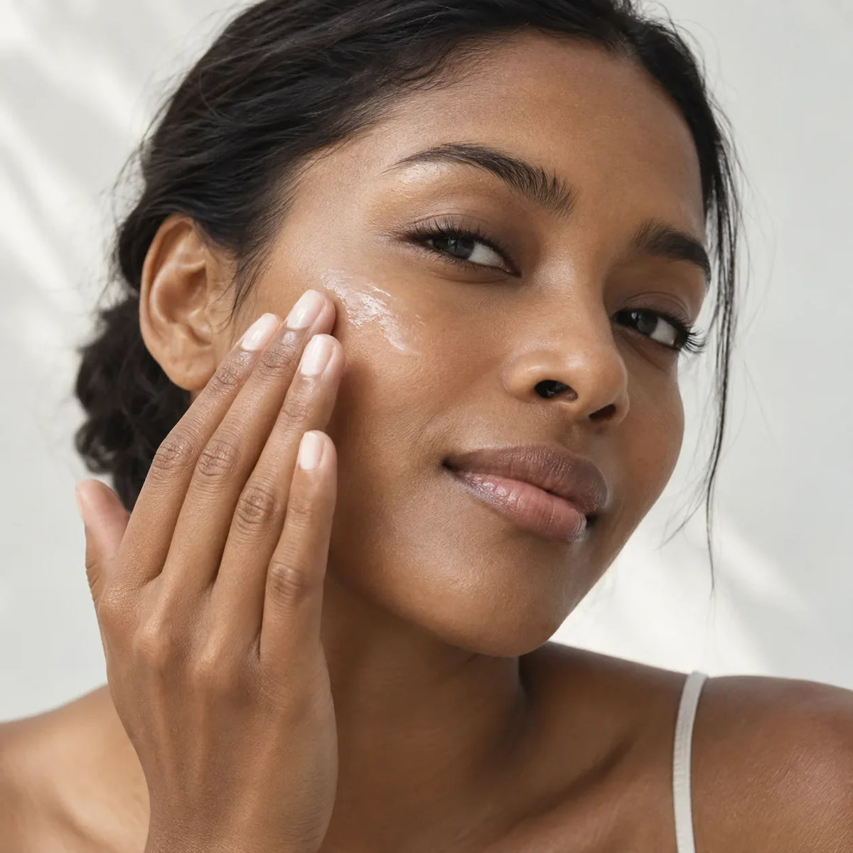 Editorial close-up of clear sunscreen being smoothed onto medium-brown skin in natural window light